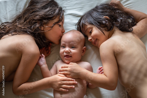 фотографія two elder sisters kissing smiling newborn sister