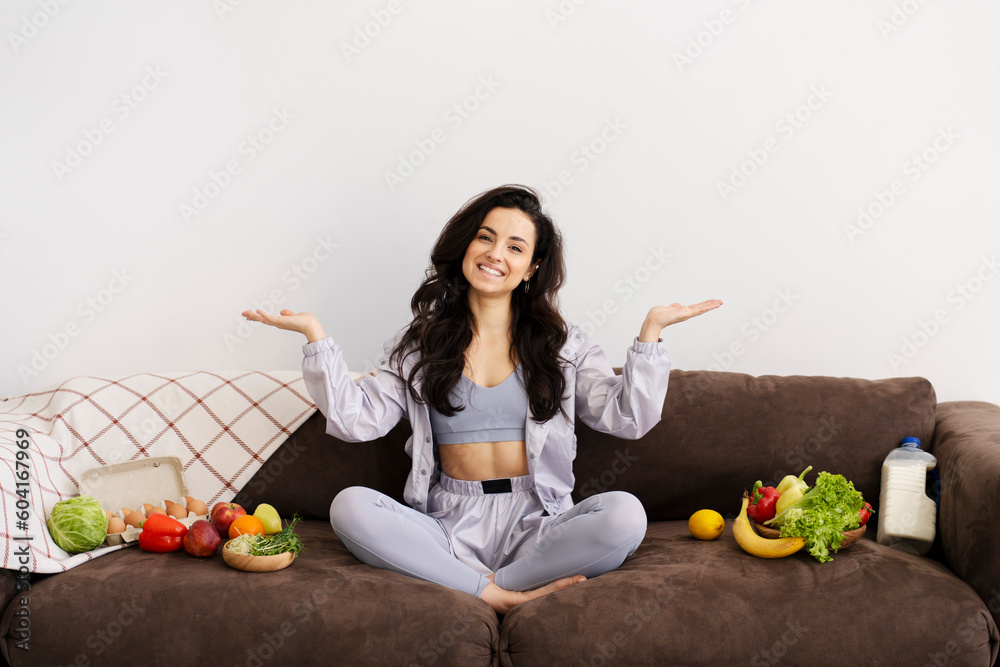 Smiling fit woman pointing hands to blank space, sitting with fruits and vegetable Smiling fit woman pointing hands to blank space, sitting with fruits and vegetable
