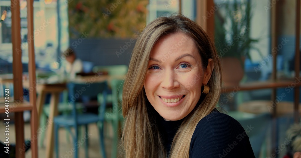 Head shot woman raise eyebrows smile openly in urban cafe with genuine interior. Straight camera