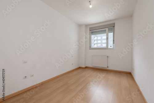 An empty room with white painted walls, a light wooden floor, a single aluminum window