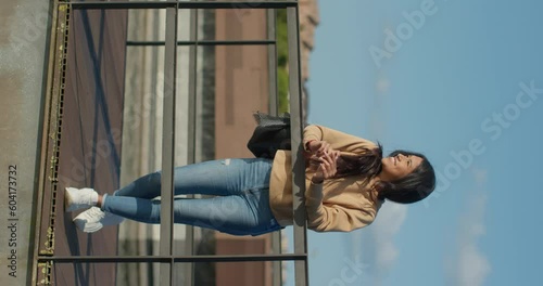 Young teenage Latina college student using social networks with her smartphone in a park, vertical shot