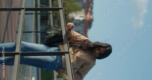 Young teenage Latina college student using social networks with her smartphone in a park, vertical shot