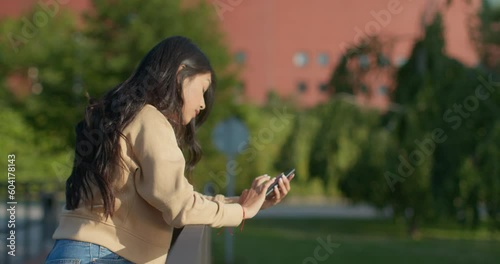 Young teenage latin college student using social networks with her smartphone in a park
