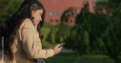 Young teenage latin college student using social networks with her smartphone in a park