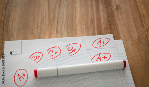 Different grades school paper marked in red ink over a wood desktop. Test results concept. Pass exam.