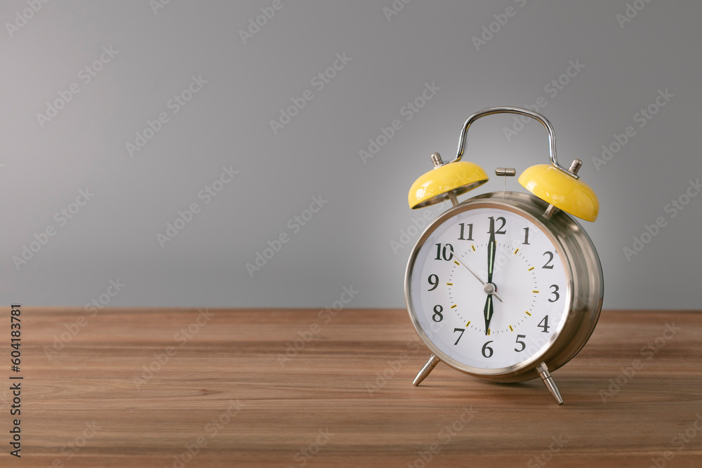 Retro silver alarm clock. 6:00.  am,  pm. Neutral background. Brown wood surface. Horizontal  photography with empty space for text or image.