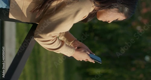 Young teenage Latina college student using social networks with her smartphone in a park, vertical shot