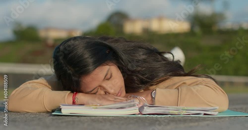 Young teenage Latina college student studying for an exam in an outdoor park with books