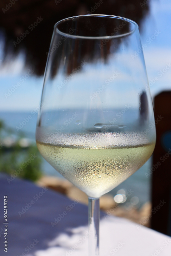 Obraz premium Glass of an ice cold vine on the table in the 2 Kitarrat Arome Deti restaurant on the Adriatic beach in Dürres, Albania. Beautiful sunny summer day. Blue sky and the sea. Selective focus