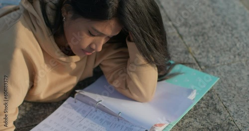 Young teenage Latina college student studying for an exam in an outdoor park with books