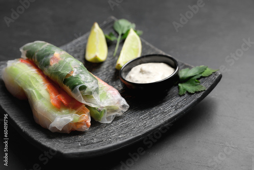 Delicious rolls wrapped in rice paper served on black table, closeup