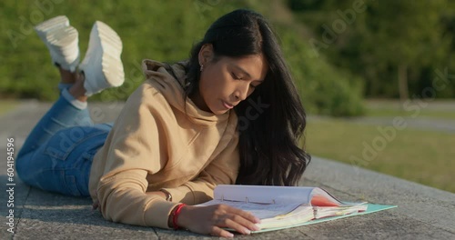 Young teenage Latina college student studying for an exam in an outdoor park with books
