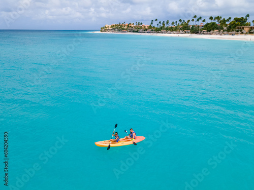 Fototapeta Naklejka Na Ścianę i Meble -  Couple Kayaking in the Ocean on Vacation Aruba Caribbean Sea, man and woman mid age kayak in ocean blue clear water with white beach and palm trees Aruba
