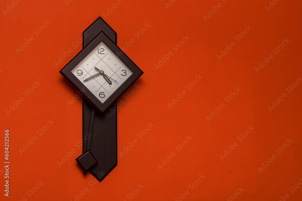 Wooden squire clock with pendulum hanging on a orange wall Wooden squire clock with pendulum hanging on a orange wall