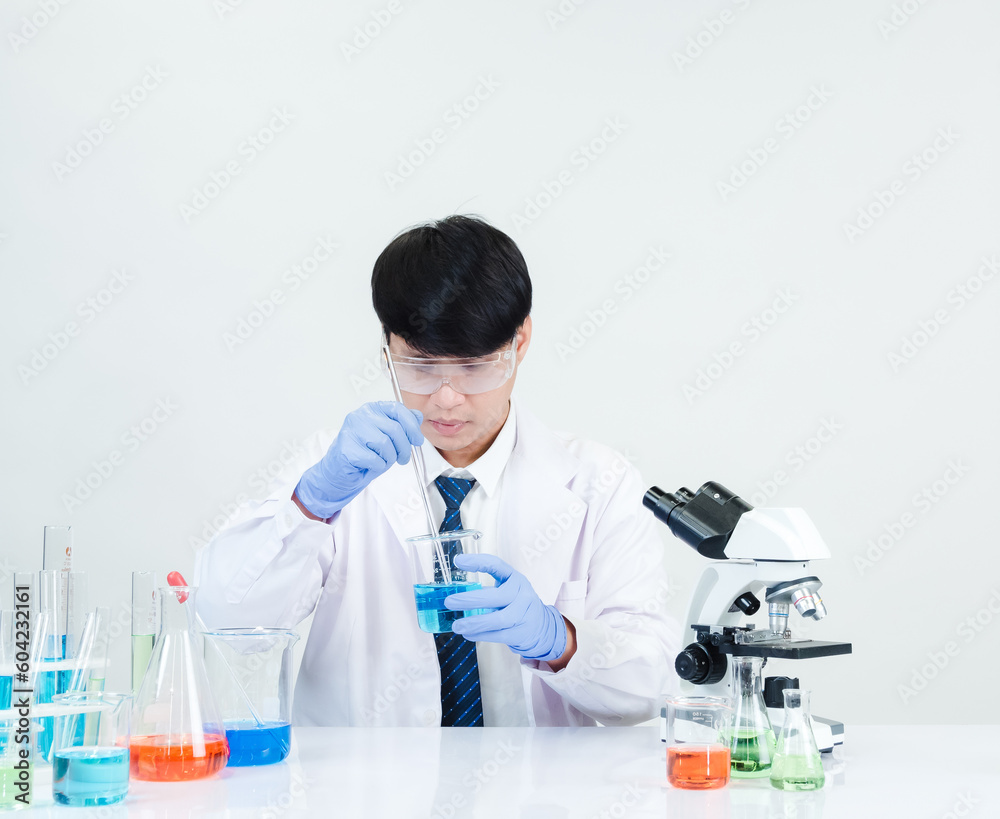 Fototapeta premium Asian male student scientist Wearing a doctor's gown in the lab looking hand at chemist. caused by mixing reagents in scientific research laboratories with test tubes and microscope on the table