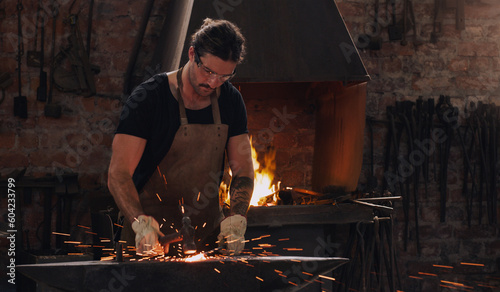 Schilderij op canvas Hammer, anvil and fire with a man working in a forge for metal work manufacturing or production