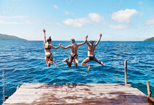 Photographie Water, back of people jumping off a pier holding hands and into the ocean together in blue sky