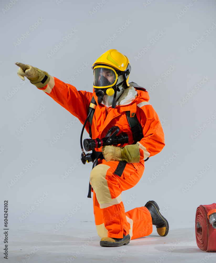 Vertical picture shows a firefighter sitting and holding a fire hose while pointing his finger sideways on a white background. Vertical picture shows a firefighter sitting and holding a fire hose while pointing his finger sideways on a white background.