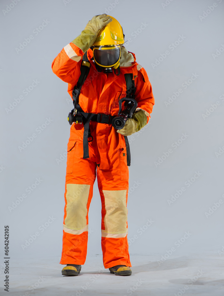 Vertical picture shows a firefighter standing and holding a fire hose while touching his yellow helmet on a white background. Vertical picture shows a firefighter standing and holding a fire hose while touching his yellow helmet on a white background.
