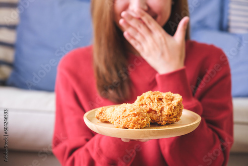 Closeup image of a happy woman covering mouth with hand  holding and looking at a plate of fried chicken