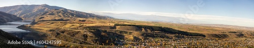 Panorama of Clyde town on a hill in a mountainous region with a river, a dam, and autumn trees.