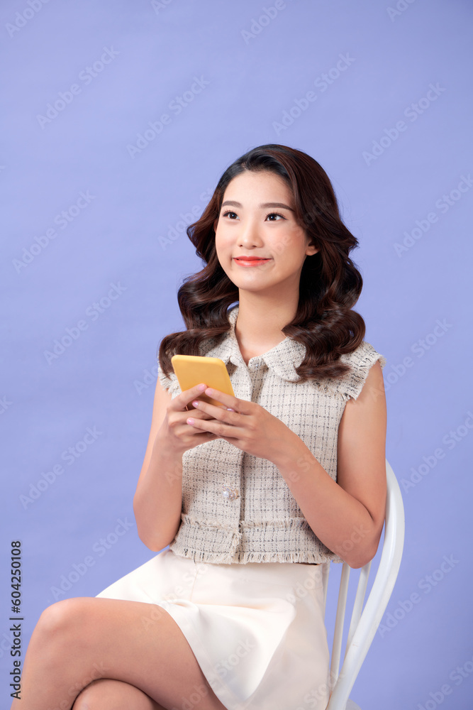 Young woman with smartphone sitting in chair on purple background Young woman with smartphone sitting in chair on purple background