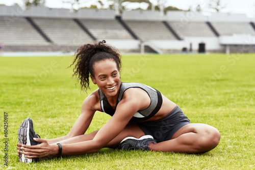 Happy woman, fitness and stretching body on grass for running, exercise or workout at the stadium. Active female person or athlete in warm up leg stretch for sports training or cardio run on a field