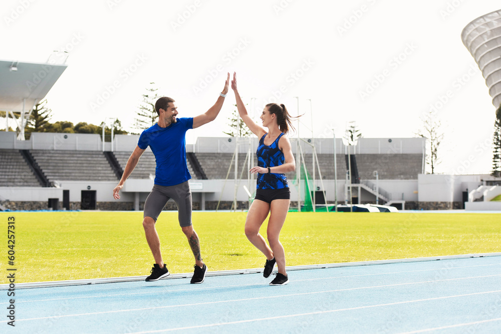 People, high five and running on stadium track for exercise, workout or training together in athletics. Man and woman touching hands in teamwork celebration for exercising, run or winning in fitness