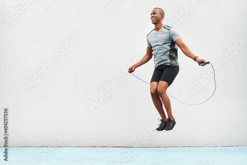 Jump, rope and space with black man skipping in stadium for sports, workout and cardio. Performance, health and body with male athlete training on track for strong, mockup and exercise by wall