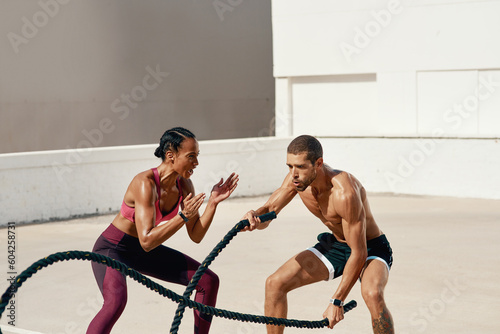 Woman, personal trainer and battle rope training for workout, exercise or fitness outdoors. Fit, active or serious coaching with man person exercising with ropes for sports endurance or motivation