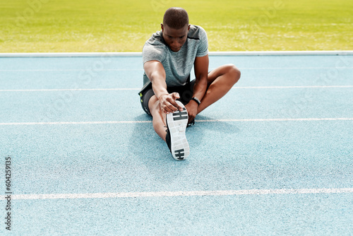 Athlete man, sitting and track for stretching legs to start training, exercise or running for fitness outdoor. African runner, warm up muscle or body for workout at stadium for race, contest or sport