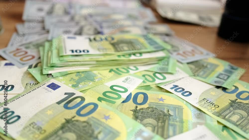 100 euros bills and American dollars slow motion close-up. Many paper money cash hundreds euro and dollar lies on wooden table. Financial management. 100 euros bills and American dollars slow motion close-up. Many paper money cash hundreds euro and dollar lies on wooden table. Financial management.