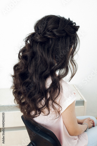 Photo of a beautiful hairstyle, from black wavy hair and a braid, on the back of the girl's head. Image for your creative decoration or design.