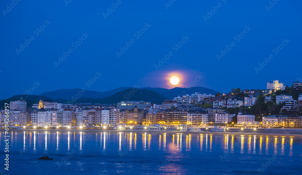 Nightfall with full moon on the beach and bay of La Concha, city of Donostia-San Sebastian, Basque Country.