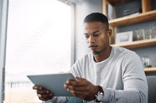 Internet, tablet and man on couch reading social media post, email or streaming video on subscription service. Scroll, search and person with serious face and checking online movie website on sofa.