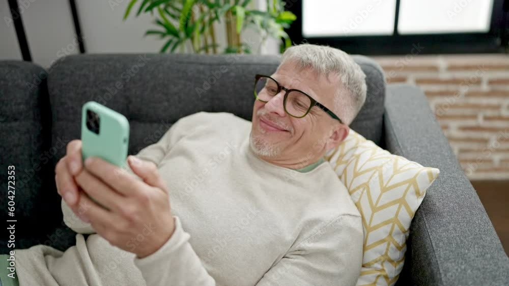 Middle age grey-haired man using smartphone lying on sofa at home Middle age grey-haired man using smartphone lying on sofa at home