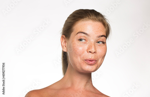 Pretty girl with freckles looks away with her hair tied up in front of the camera on a white background