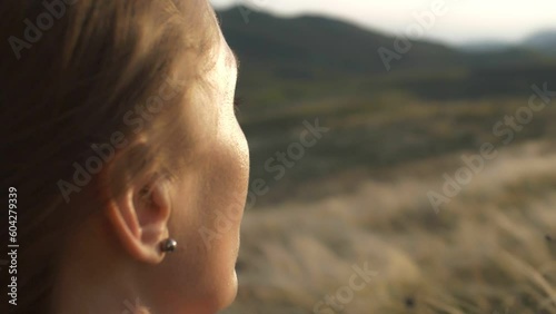 A profile portrait of a woman admiring a mountain landscape in the sun glare sitting against the backdrop of a feather grass shining in the rays of a sunset. Back and side view slow motion closeup photo