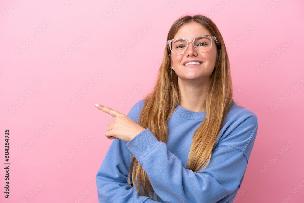 Young blonde woman isolated on pink background With glasses and pointing side Young blonde woman isolated on pink background With glasses and pointing side
