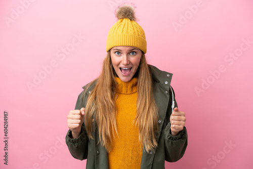 Young blonde woman wearing winter jacket isolated on pink background celebrating a victory in winner position