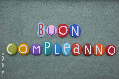 Buon compleanno, italian Happy Birthday text composed with multi colored stone letters over green sand