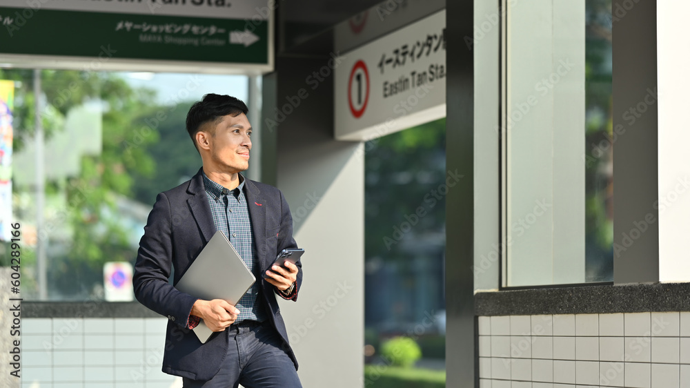 Fototapeta premium Businessman in full suit using smartphone in subway station during his morning commute