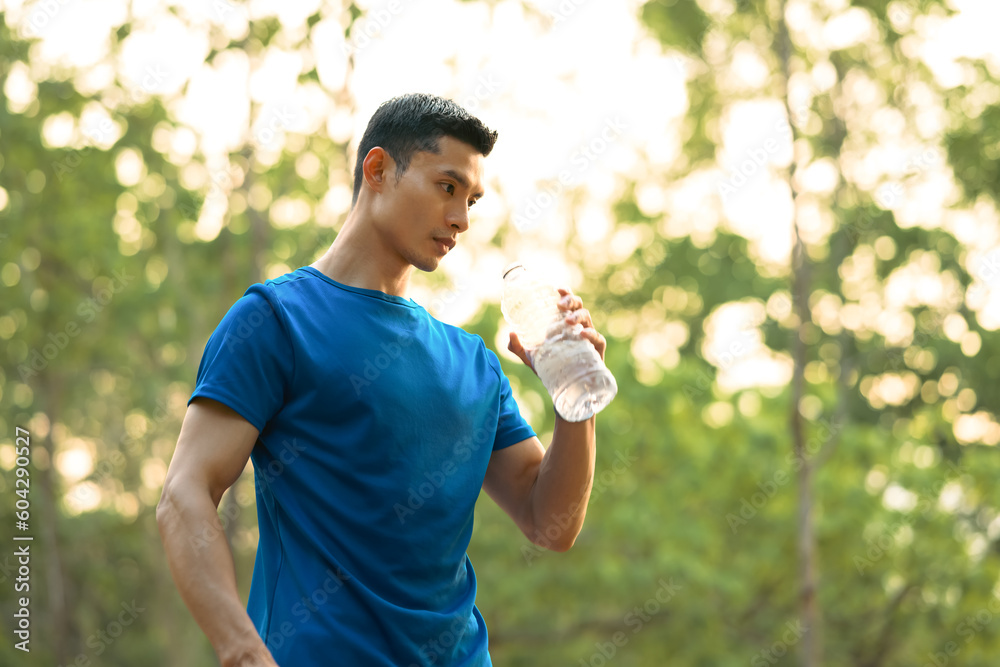 Asian male runner drinking water from bottle, resting after workout session at sunny morning. Fitness, training and healthy lifestyle Asian male runner drinking water from bottle, resting after workout session at sunny morning. Fitness, training and healthy lifestyle