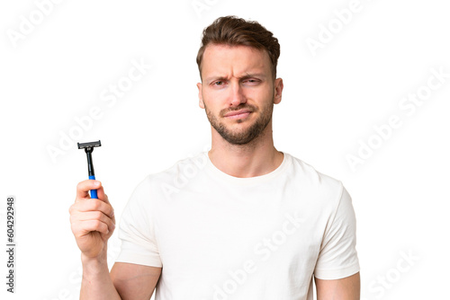 Young caucasian man shaving his beard over isolated chroma key background with sad expression