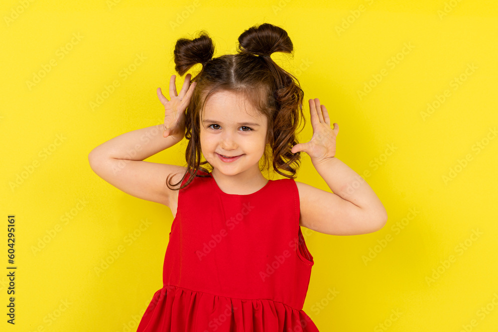 Cute little surprised happy girl in a red dress stands on a yellow background. card, banner. lifestyle. space for text. High quality photo Cute little surprised happy girl in a red dress stands on a yellow background. card, banner. lifestyle. space for text. High quality photo