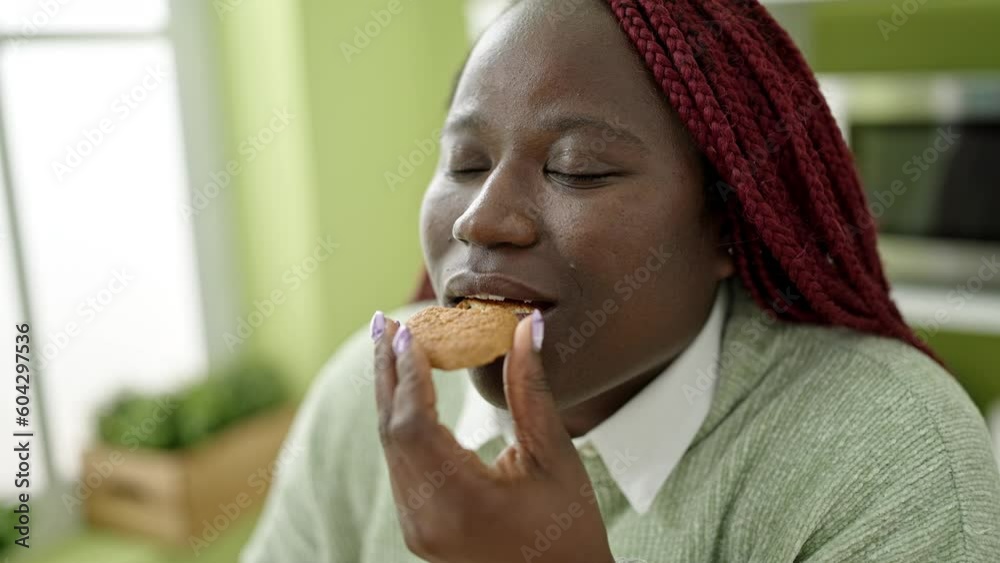 African woman with braided hair eating cookie with closed eyes at dinning room African woman with braided hair eating cookie with closed eyes at dinning room