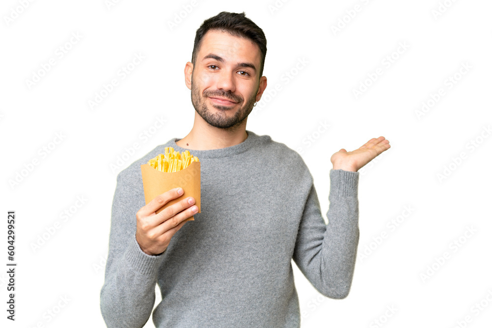 Young caucasian man holding fried chips over isolated chroma key background extending hands to the side for inviting to come Young caucasian man holding fried chips over isolated chroma key background extending hands to the side for inviting to come