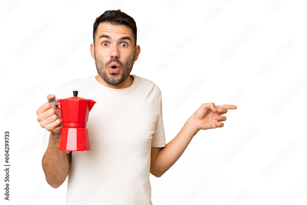Young caucasian man holding coffee pot over isolated chroma key background surprised and pointing side Young caucasian man holding coffee pot over isolated chroma key background surprised and pointing side