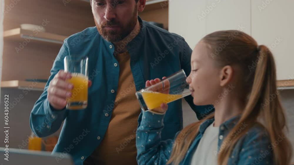 Caucasian father with little daughter child girl drinking fresh drink healthy tasty orange juice healthcare dad help using laptop teach browsing computer kid happy family dinner breakfast at kitchen
