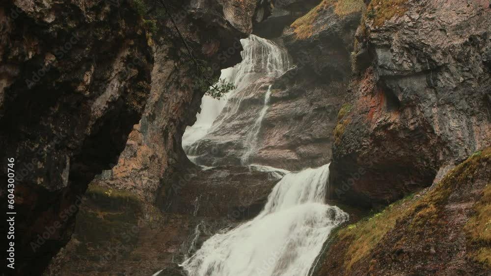Cascada rodeada de montañas en un estrecho cañón bajo la lluvia y bruma. Cascada rodeada de montañas en un estrecho cañón bajo la lluvia y bruma.